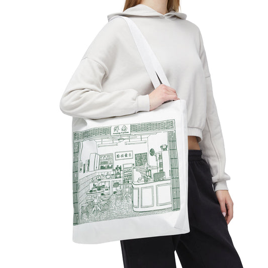 Person wearing a white hoodie holding a tote bag with a green illustration of a store.